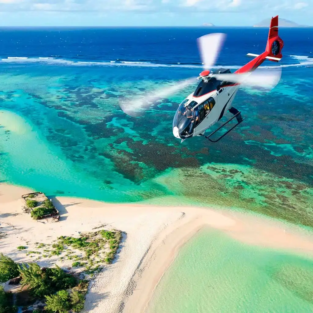 Helicopter above a turquoise coastal lagoon, sandy shoreline, reef patterns and the open sea.