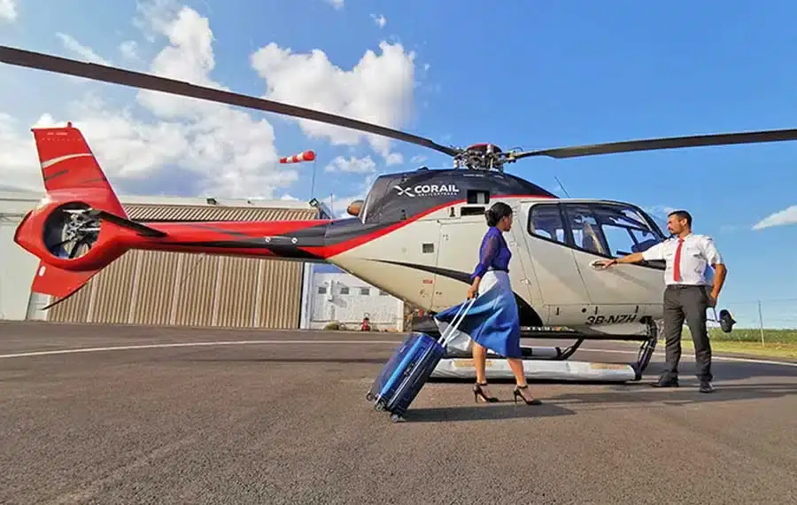 A passenger approaching a helicopter with assistance on a paved apron beside an aircraft hangar.